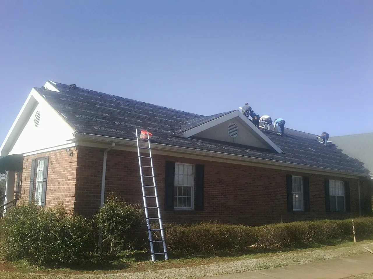 Crew tearing shingles off a brick ranch roof with a ladder set — Metal Roof Repair work by our crew in Union Hall