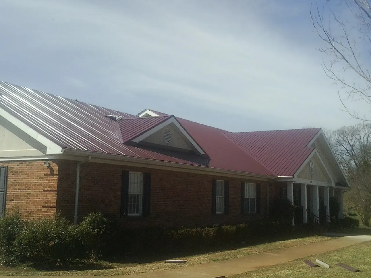 Red metal roof with gabled entries on a long brick building, from a Hail Damage Roof Repair job in Union Hall