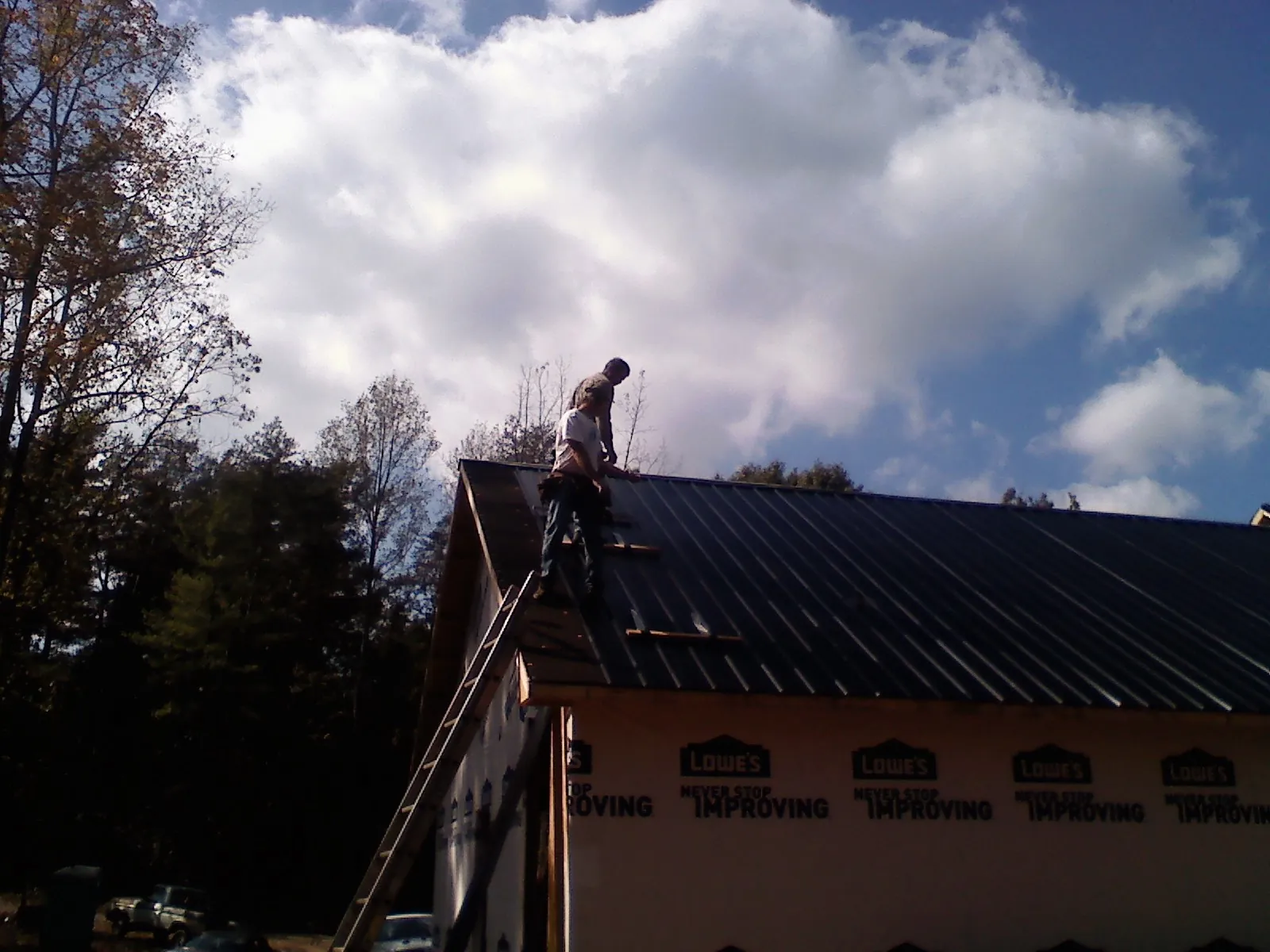 Roofer fastening dark metal panels high against a cloudy sky, from a Roof Inspection job in Union Hall