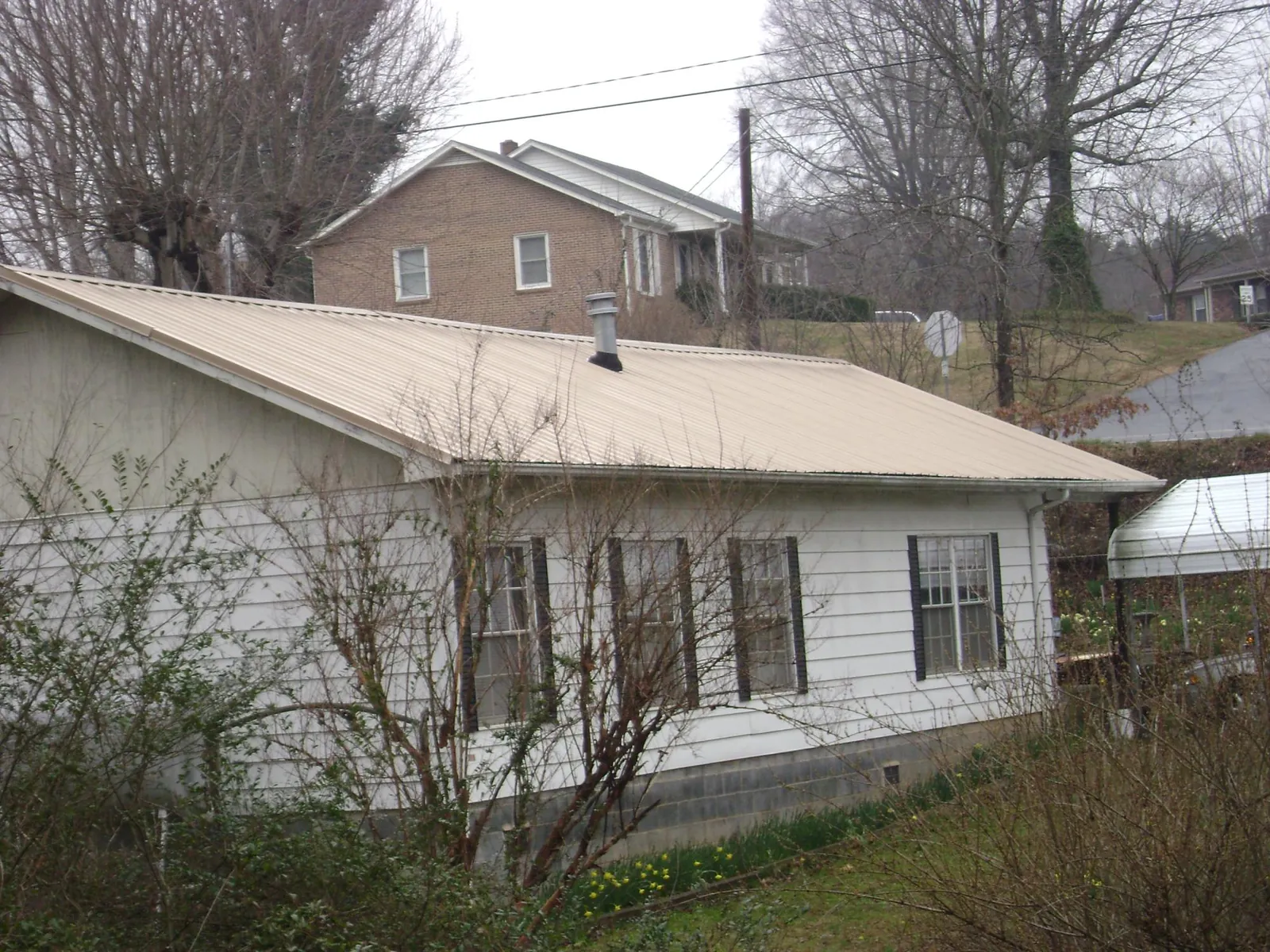 Tan metal roof on a white sided house set into a hillside — Commercial Roofing by Roofing Brothers in Union Hall